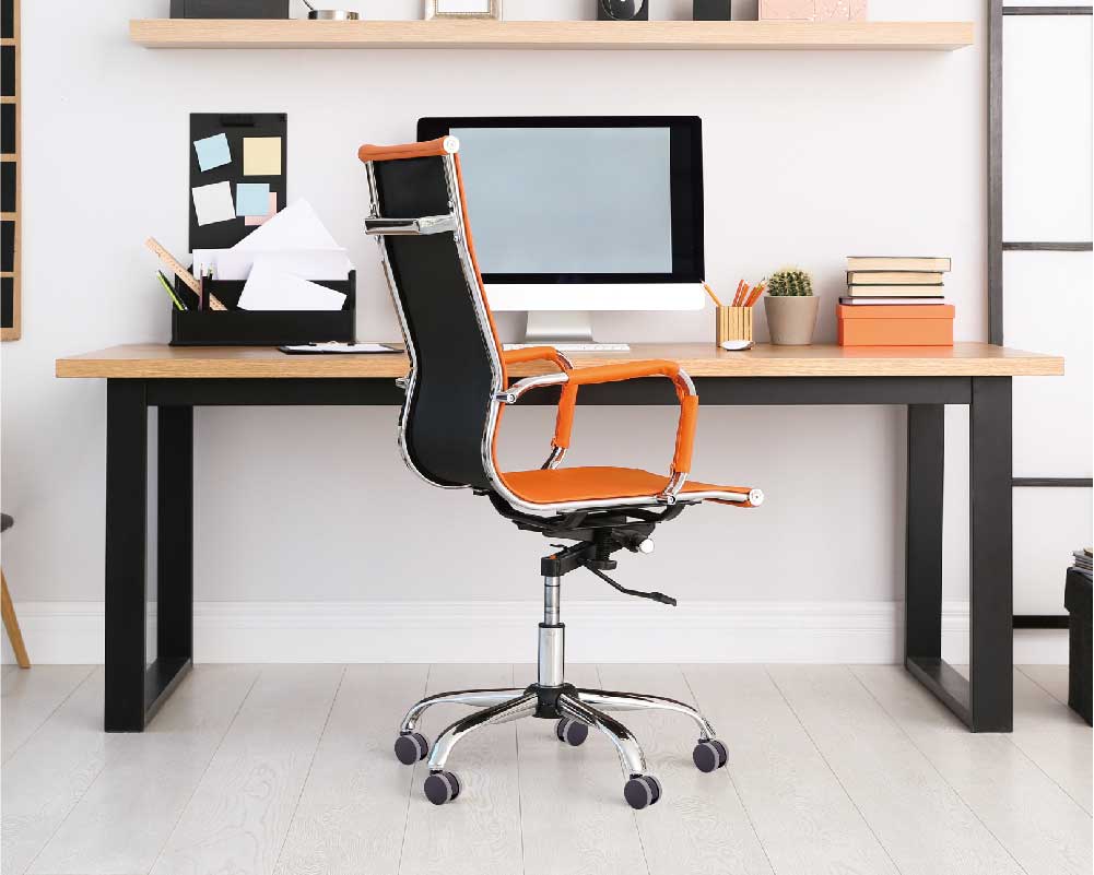 Modern office setup with a black and orange ergonomic chair on caster wheels in front of a wooden desk with a computer and office supplies