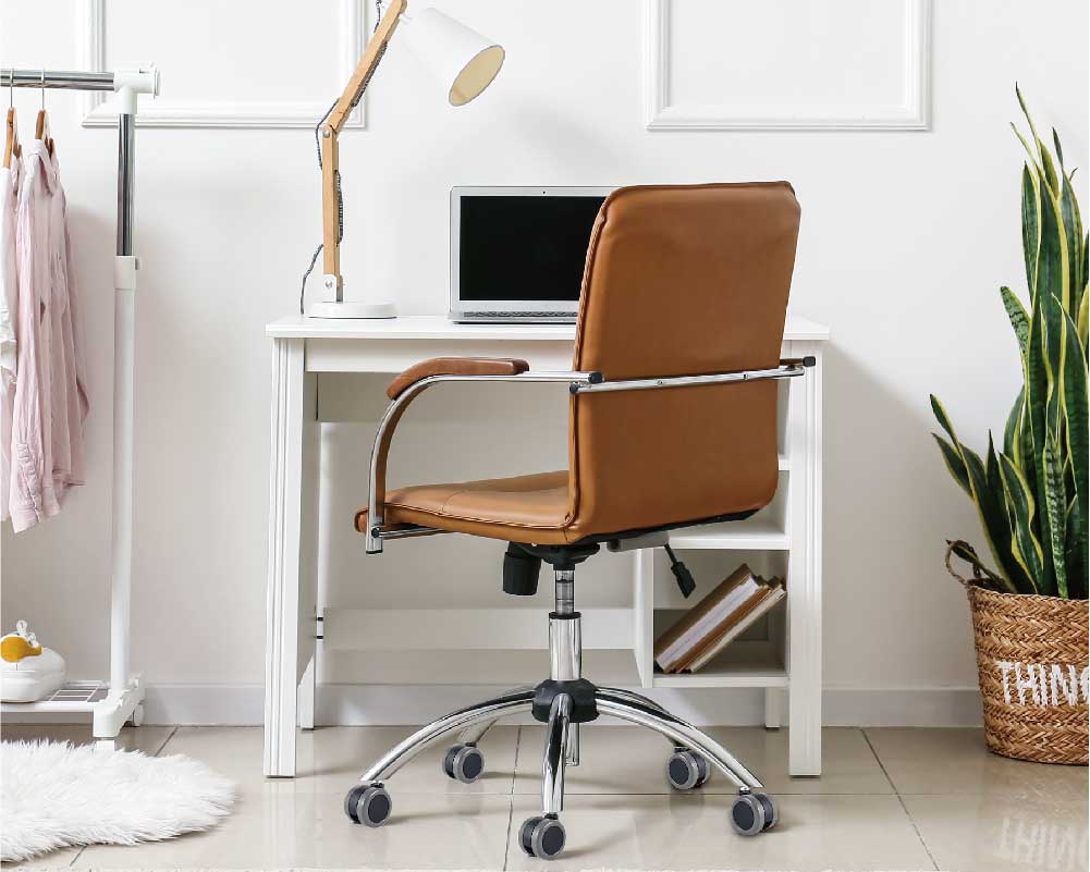Modern office setup with a black and orange ergonomic chair on caster wheels in front of a wooden desk with a computer and office supplies.