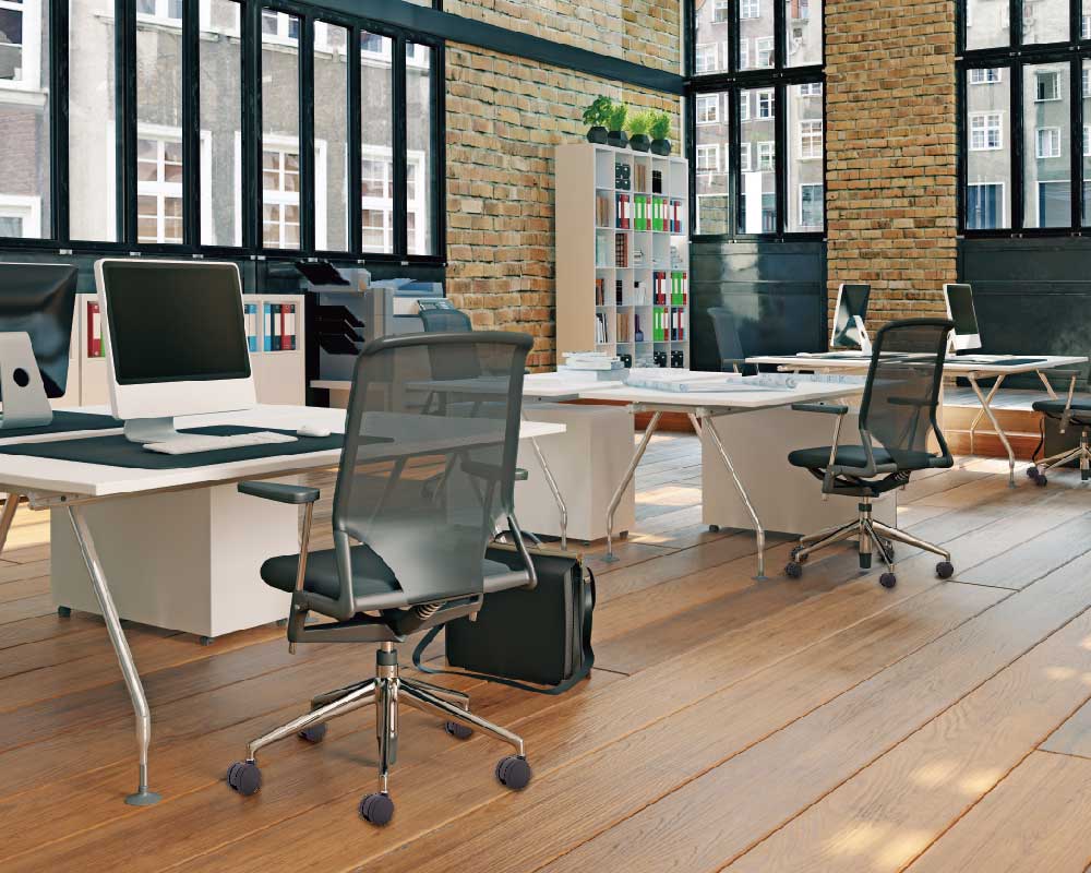 Modern office space with large windows, featuring desks and black office chairs with caster wheels arranged neatly in rows